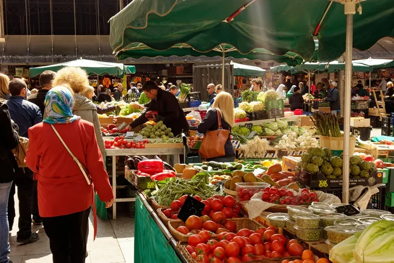 Pomodori e carciofi sui banchi, sotto gli ombrelloni verdi